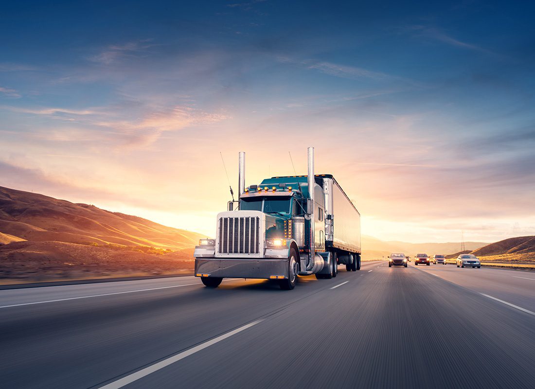 Transportation Insurance - View of a Semi Tractor Trailer Truck Driving Alongside Cars on a Large Scenic Highway at Sunset