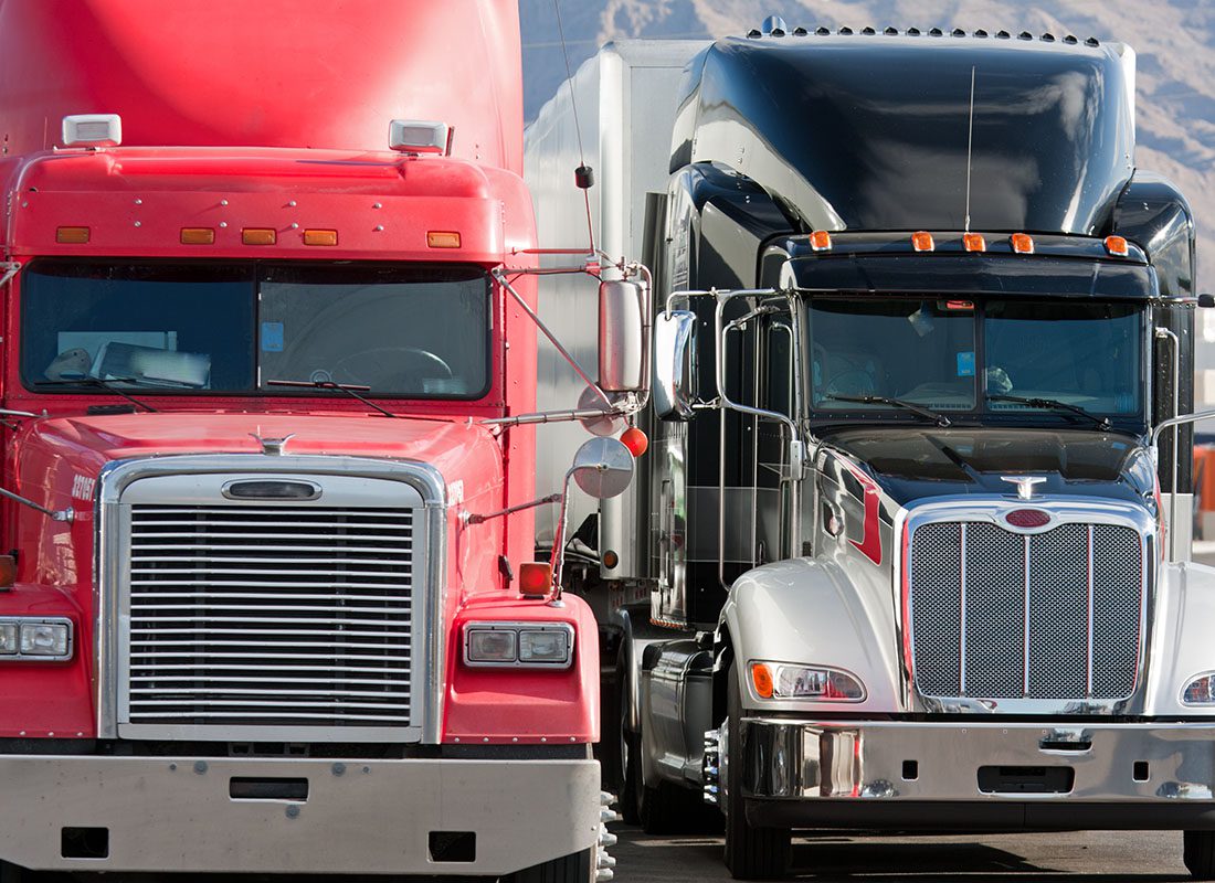 Trucking Insurance - Closeup View of Two Tractor Trailer Semi Trucks with Trailers Driving on the Highway